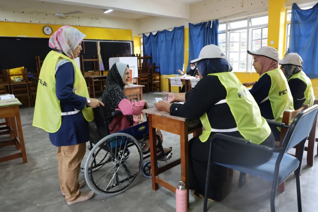 Voter in wheelchair voting in an election assisted by election staffers.